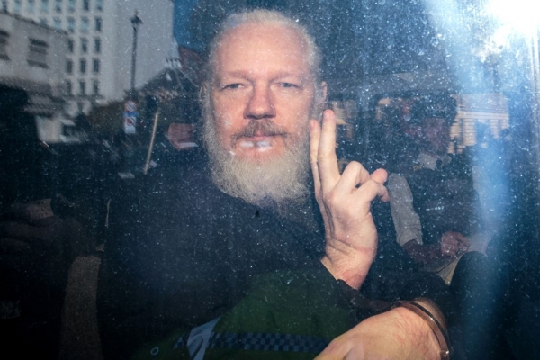Julian Assange gestures to the media from a police vehicle on his arrival at Westminster Magistrates court on April 11, 2019 in London, England. / JACOBIN