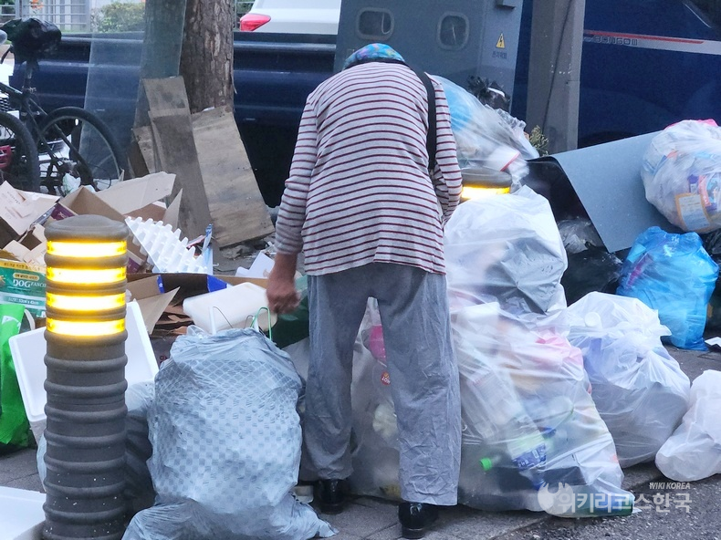 성남시 산성대로 지하철 8호선 남한산성역 입구에서 한 60대 여성 노인이 쓰레기 더미에서 플라스틱 쓰레기를 고르고 있다. [출처=위키리크스한국]